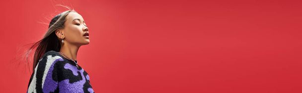 гарна азіатська дівчина в яскравому светрі з тваринним принтом з кольє у формі серця на червоному, банер - Фото, зображення
