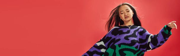 young asian girl in vibrant sweater with animal print with heart shaped necklace on red, ease banner - Photo, Image