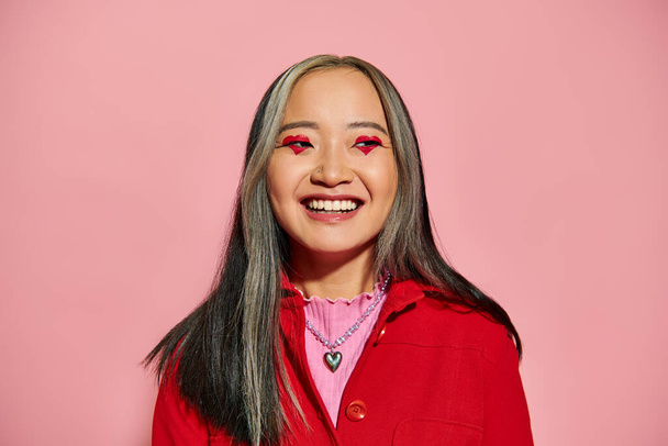 Valentim dia conceito, alegre asiático mulher com coração em forma de olho maquiagem posando em rosa pano de fundo - Foto, Imagem