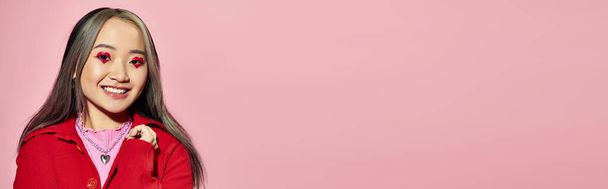 Банер дня Святого Валентина, весела азіатка з макіяжем у формі серця позує на рожевому тлі - Фото, зображення