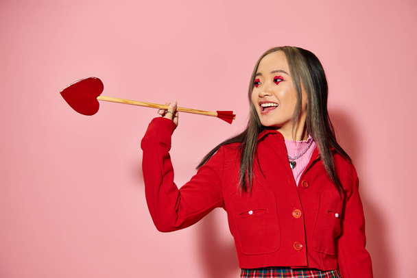 Walentynki koncepcja, wesoła azjatycka kobieta z makijażem w kształcie serca trzymając strzałkę na różowy - Zdjęcie, obraz