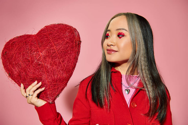 Valentin nap, vidám ázsiai nő élénk szem smink tartja piros szív rózsaszín háttér - Fotó, kép