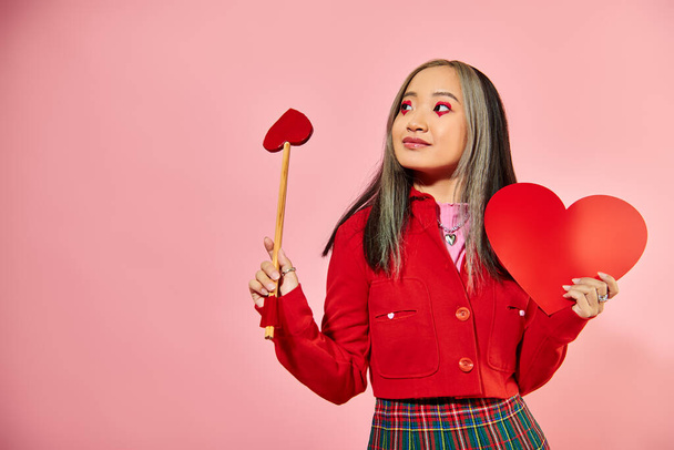 San Valentín día, feliz chica asiática con vibrante ojo maquillaje celebración de cartón corazón en rosa telón de fondo - Foto, Imagen