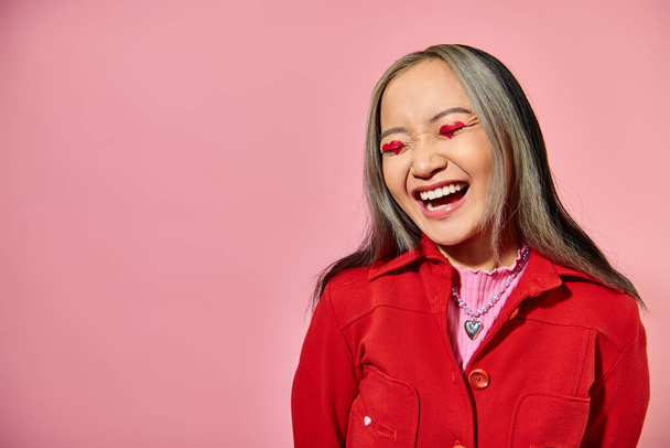 Valentim dia conceito, feliz asiático mulher com coração olho maquiagem rindo no fundo rosa - Foto, Imagem