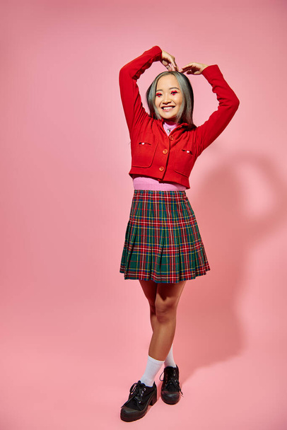 Valentim dia conceito, menina asiática feliz em casaco vermelho mostrando coração com as mãos no fundo rosa - Foto, Imagem