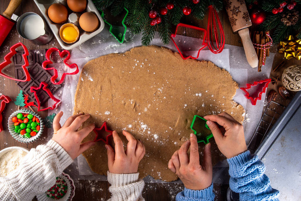 Cooking Christmas cookies family background. Mother and daughter hands top view on cozy wooden background, making gingerbread biscuits with cookie cutters, with New Year Christmas decoration - Photo, Image