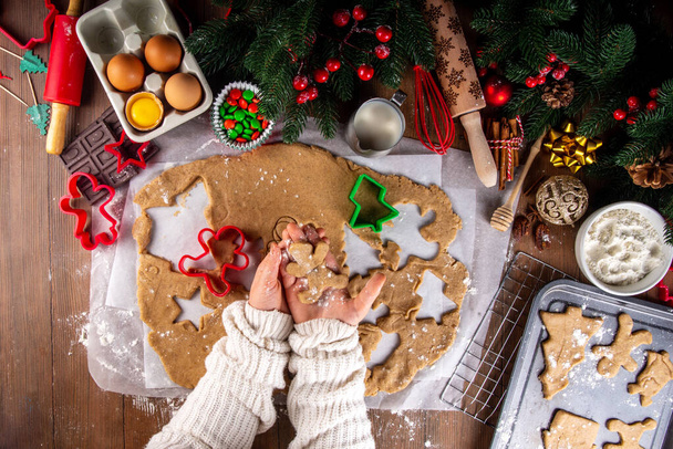 Cooking Christmas cookies family background. Mother and daughter hands top view on cozy wooden background, making gingerbread biscuits with cookie cutters, with New Year Christmas decoration - Photo, Image