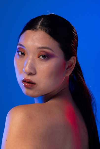 Portrait of asian woman with black hair wearing purple eye shadow on blue background. Cosmetics, makeup, female fashion and beauty, unaltered. - Foto, imagen