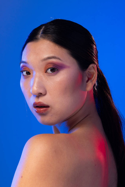Portrait of asian woman with black hair wearing purple eye shadow on blue background. Cosmetics, makeup, female fashion and beauty, unaltered. - Valokuva, kuva