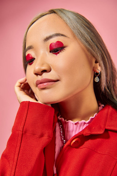 portrait de songeur asiatique jeune femme avec coeur forme maquillage des yeux regardant loin sur fond rose - Photo, image