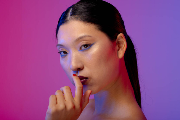 Portrait of asian woman wearing blue eyeliner and red nail polish on purple background. Cosmetics, makeup, female fashion and beauty, unaltered. - Photo, image