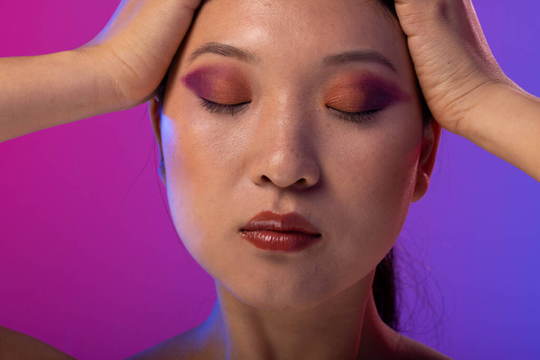 Asian woman with black hair wearing purple eye shadow and red lipstick on purple background. Cosmetics, makeup, female fashion and beauty, unaltered. - Φωτογραφία, εικόνα