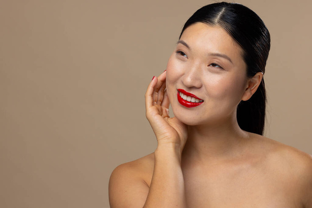 Asian woman wearing red lipstick and nail polish on beige background, copy space. Cosmetics, makeup, female fashion and beauty, unaltered. - Zdjęcie, obraz