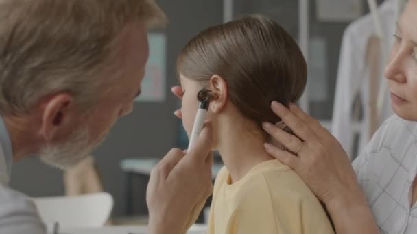 Brustkorb eines professionellen männlichen HNO-Arztes, der Ohren eines asiatischen Mädchens untersucht, Arztbesuch mit Mutter in moderner Klinik - Filmmaterial, Video