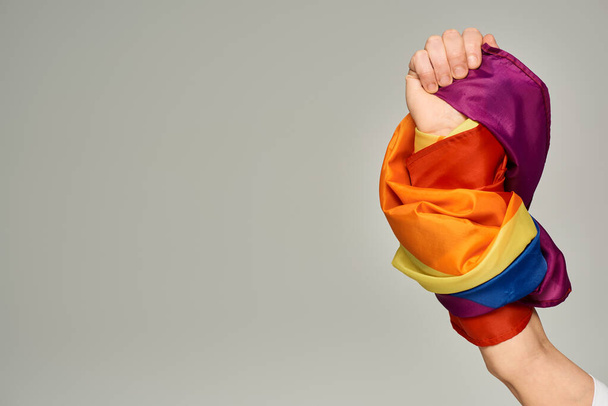 cropped view of hand of non-binary person holding LGBT flag on grey backdrop with copy space - Photo, Image