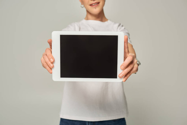 vue recadrée de la personne queer en t-shirt blanc montrant tablette numérique avec écran blanc sur gris - Photo, image