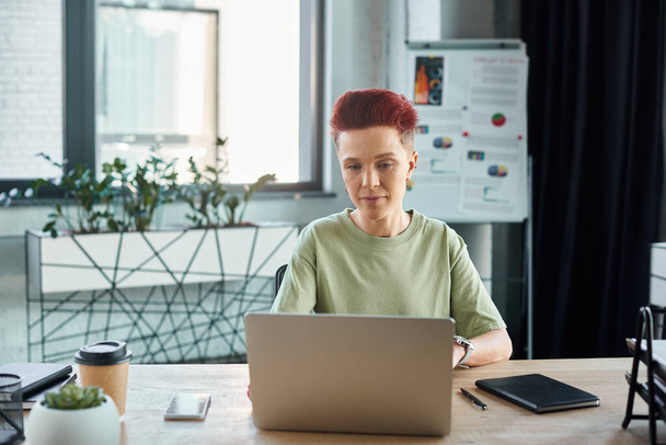 geconcentreerde bigender manager werkt op laptop in de buurt van koffie te gaan op het bureau in modern kantoor - Foto, afbeelding