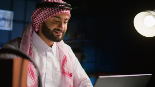 Muszlim teleportáló távolról dolgozik félhomályos lakás alkotó e-maileket laptopon. Közel-keleti dolgozó otthon gépelés üzleti adatok notebook eszköz, visel hagyományos öltözék, közelről - Felvétel, videó