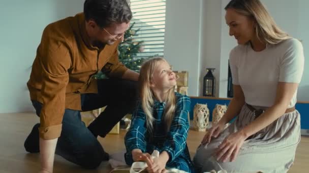 Caucasian girl wrapping Christian present on her own and parents helping her. Shot with RED helium camera in 8K.     - Footage, Video