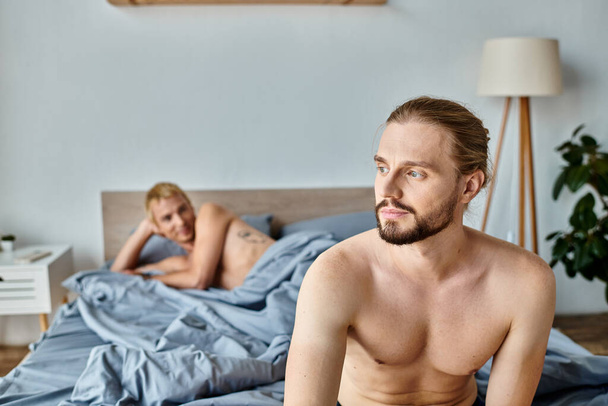 мечтательный и позитивный бородатый мужчина, глядя в сторону гей-партнер лежит на кровати, счастье и спокойствие - Фото, изображение