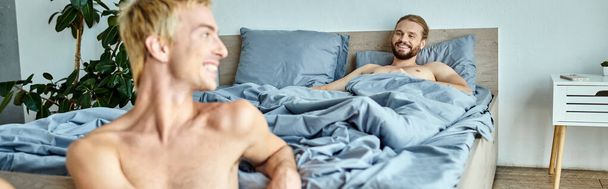 radosny brodaty gej człowiek leżący na łóżko i patrząc na uśmiechnięty chłopak rano horyzontalny sztandar - Zdjęcie, obraz