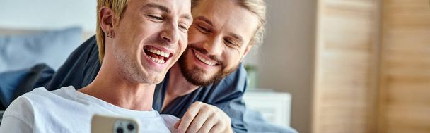 alegre tatuado gay hombre navegación internet en smartphone cerca sonriente novio en dormitorio, banner - Foto, imagen