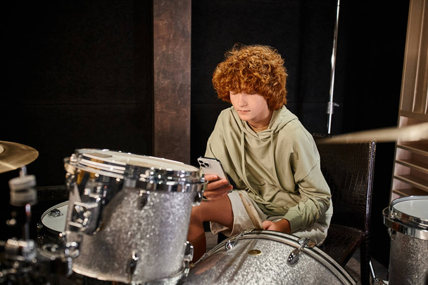 концентрированный милый рыжий подросток в повседневной удобной одежде, играющий на барабанах в студии - Фото, изображение