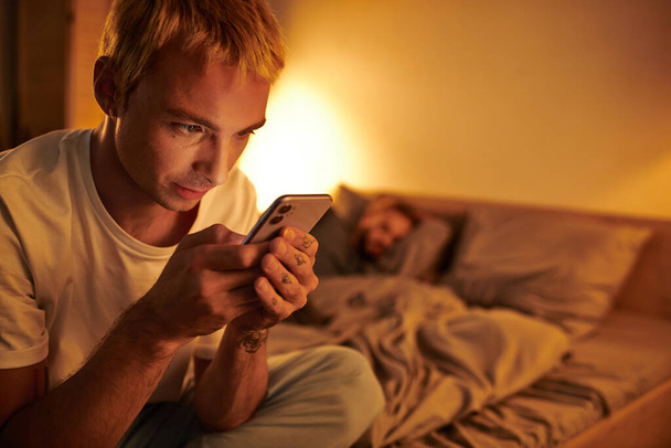 ベッドルームで夜寝ているボーイフレンドの近くの携帯電話で忠実なゲイのマネージャーメッセージ - 写真・画像