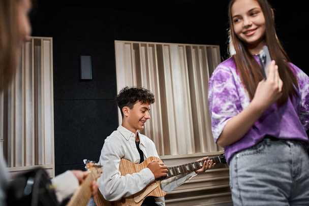 suloinen teini-ikäinen poika hammasraudat rento asu kitaransoitto vieressä hänen ystävänsä, musiikkiryhmä - Valokuva, kuva