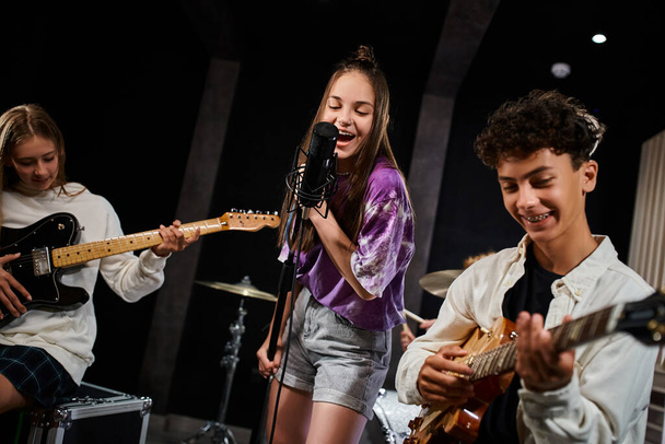 веселые очаровательные подростки в повседневных одеждах, поющие и играющие на инструментах в студии, музыкальной группе - Фото, изображение