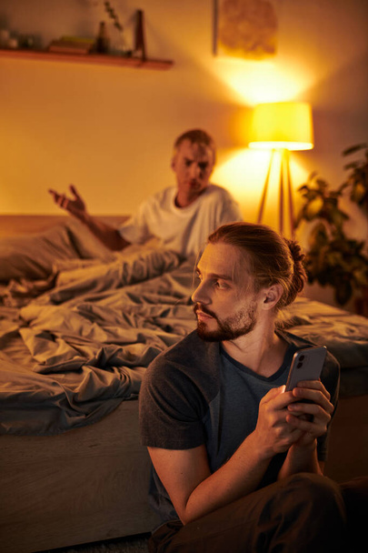 niezadowolony gej człowiek kłótnia z chłopak wiadomości na smartfon w nocy w sypialnia kłopoty - Zdjęcie, obraz