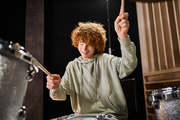 joyous talented teenage boy with red hair in everyday cozy attire playing his drums actively - Photo, Image