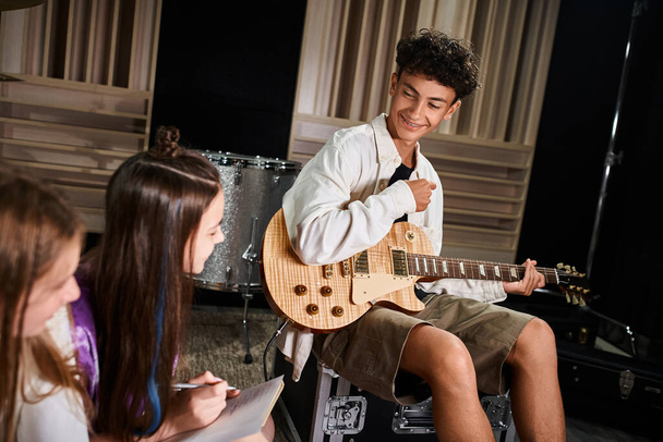 focus op vrolijke schattige tiener jongen met beugels vasthouden van gitaar en kijken naar zijn wazig bandleden - Foto, afbeelding