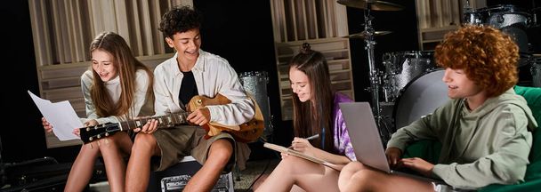 jolly teenage kapela členové v ležérní oblečení sedí s kytarou a notebookem psaní textů, banner - Fotografie, Obrázek