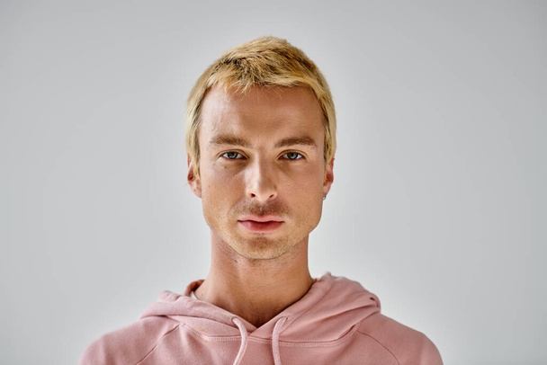 πορτρέτο του χαρισματικού άνδρα με βαμμένα ξανθά μαλλιά κοιτάζοντας κάμερα σε γκρι φόντο, μοντέρνο στυλ - Φωτογραφία, εικόνα