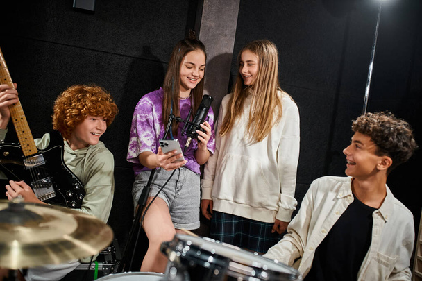 vrolijk schattig tiener meisjes zingen en glimlachen terwijl jongens spelen gitaar en drums in de studio - Foto, afbeelding