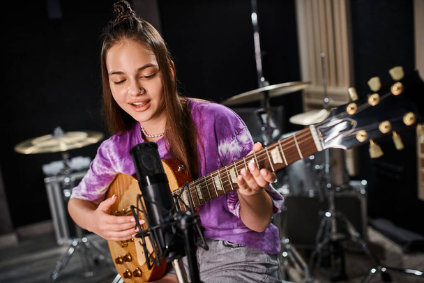 αξιολάτρευτη έφηβη κιθαρίστρια με ζωντανή casual ενδυμασία που τραγουδάει κιθάρα και τραγούδι - Φωτογραφία, εικόνα