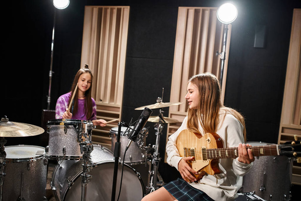 dwie utalentowane nastolatki w luźnych strojach grające na gitarze i perkusji, grupa muzyczna - Zdjęcie, obraz