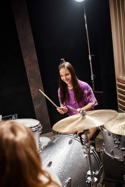joyeux jolie adolescente en vêtements vibrants jouer de la guitare et sourire heureux en studio - Photo, image