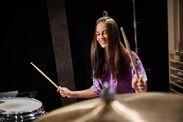 весёлая талантливая очаровательная девочка-подросток в повседневной смелой одежде, играющая на барабанах в студии - Фото, изображение