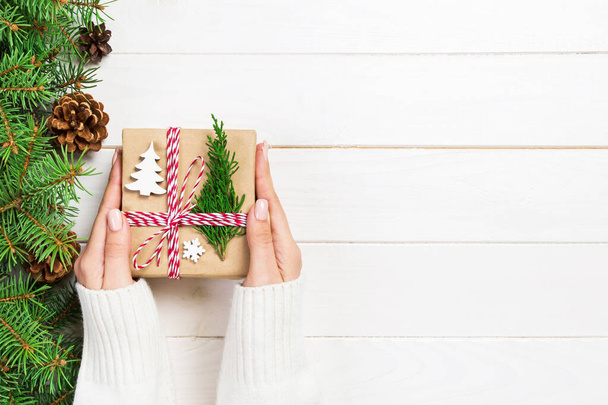 Γυναίκα χέρια δίνουν τυλιγμένο χριστουγεννιάτικο χειροποίητο δώρο σε χαρτί με Χριστουγεννιάτικη διακόσμηση. Παρόν πλαίσιο σε διακοπές στο σκοτεινό ξύλινο τραπέζι, το top view. - Φωτογραφία, εικόνα
