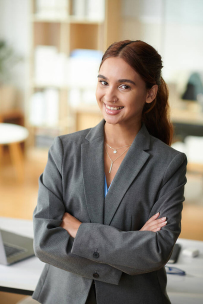 Πορτρέτο της νεαρής χαμογελαστή επιχειρηματίας με αυτοπεποίθηση που στέκεται στο γραφείο - Φωτογραφία, εικόνα