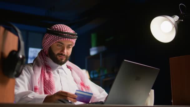 Щасливий арабський чоловік робить інтернет-магазин на комп'ютері, витрачаючи гроші на легкі речі. Посміхаючись Близький Схід людина додає метод оплати на веб-сайті для того, щоб придбати продукти - Кадри, відео
