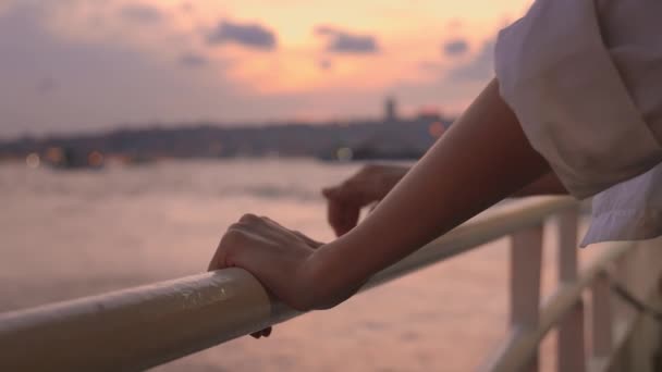 Este vagy éjszaka nem fókuszált női kezek közelsége az isztambuli kompon, miközben a Bosphorus-on pihennek. Egy lány a hajón. Hullámok és fények a város híd a háttérben. Városnéző hajó Törökországban - Felvétel, videó