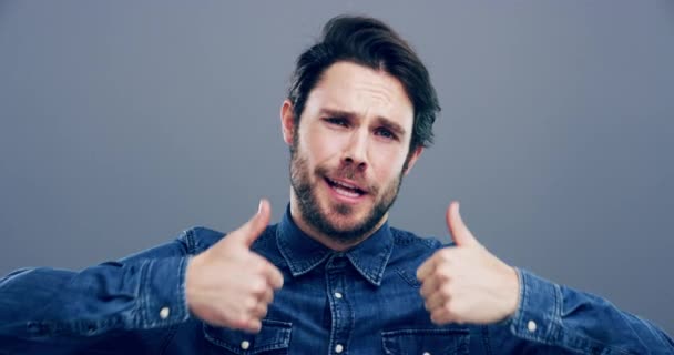 Happy man, thumbs up and winning for good job, thank you or success against a studio background. Portrait of young friendly male person or model smile and showing like emoji, yes sign or OK on mockup. - Footage, Video