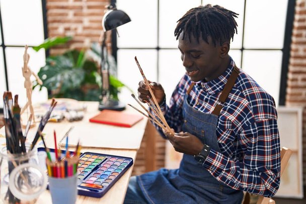 Artista afroamericano uomo sorridente fiducioso tenendo pennelli allo studio d'arte - Foto, immagini