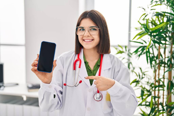 Молодая латиноамериканка доктор женщина показывает смартфон экран указывая пальцем на один самодовольный счастливый и гордый  - Фото, изображение