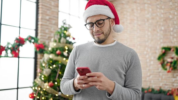 Spanyol férfi visel karácsonyi kalap okostelefon otthon - Fotó, kép