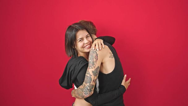 Hermosa pareja sonriendo confiada abrazándose unos a otros sobre un fondo rojo aislado - Foto, imagen