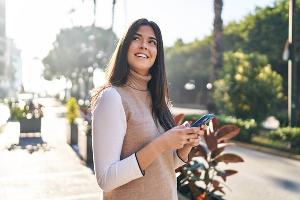 Giovane bella donna ispanica sorridente fiducioso utilizzando smartphone in strada - Foto, immagini